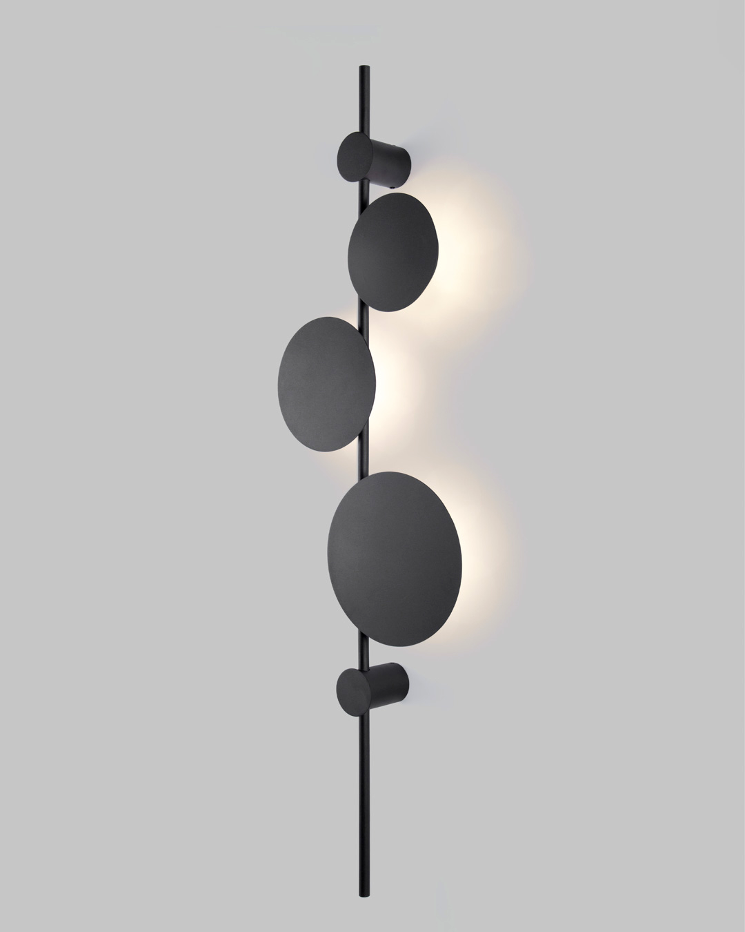 Vertical trio wall lamp with three circular elements creating soft ambient lighting / مصباح حائط عمودي بثلاث وحدات دائرية يوفّر إضاءة هادئة ولمسة فنية