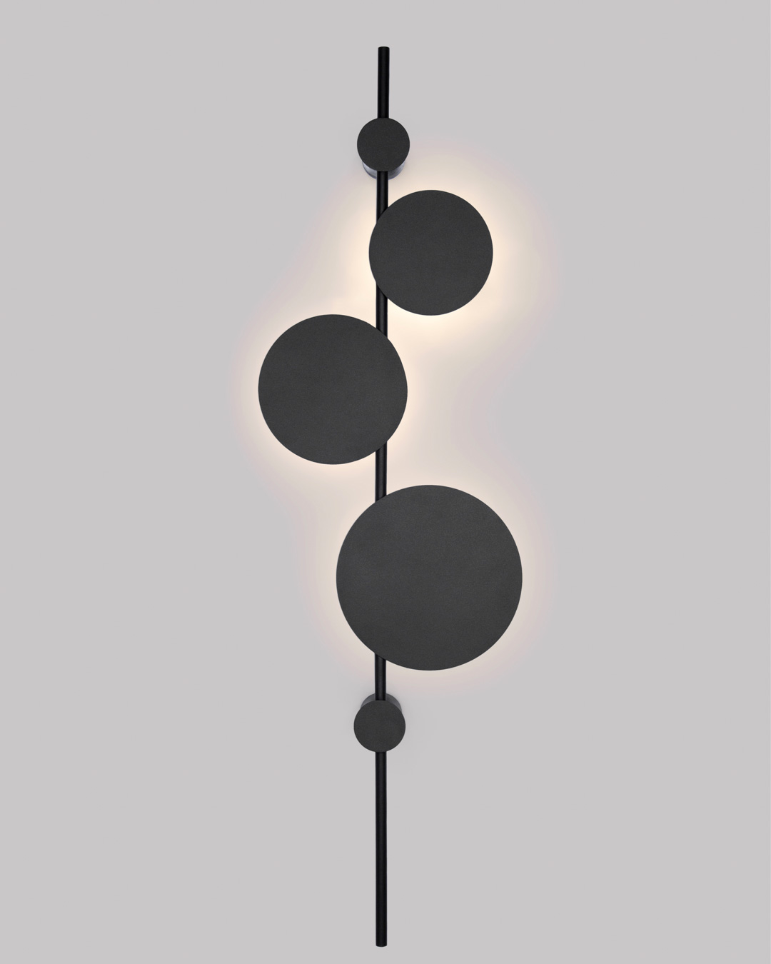 Vertical trio wall lamp with three circular elements creating soft ambient lighting / مصباح حائط عمودي بثلاث وحدات دائرية يوفّر إضاءة هادئة ولمسة فنية