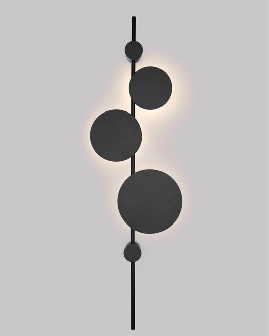 Vertical trio wall lamp with three circular elements creating soft ambient lighting / مصباح حائط عمودي بثلاث وحدات دائرية يوفّر إضاءة هادئة ولمسة فنية