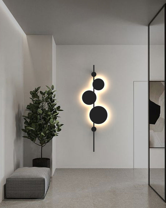 Vertical trio wall lamp with three circular elements creating soft ambient lighting / مصباح حائط عمودي بثلاث وحدات دائرية يوفّر إضاءة هادئة ولمسة فنية